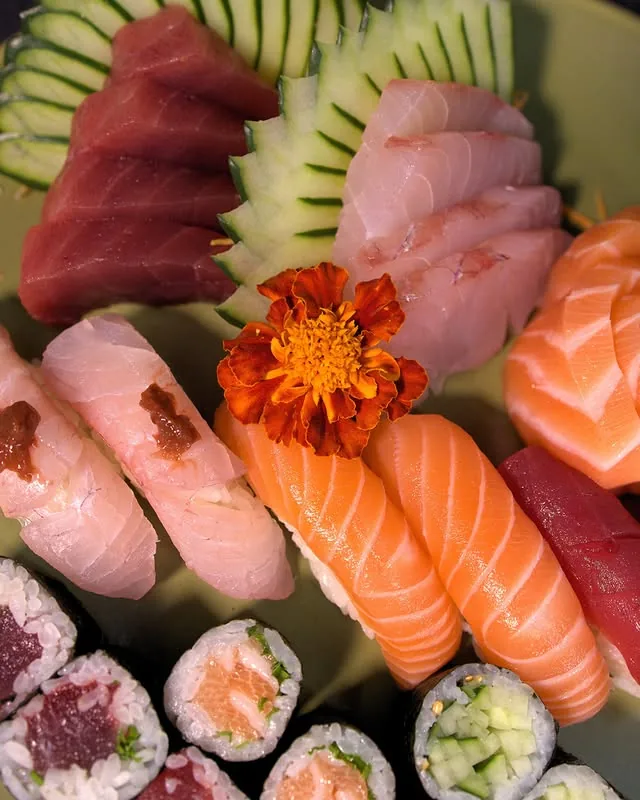 Travessa com sashimis, niguiris e rolinhos variados decorada com flor