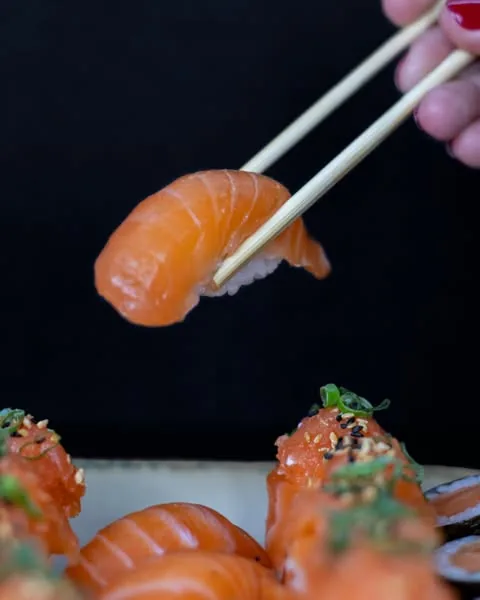 Niguiri de salmão segurado por hashi sobre fundo escuro