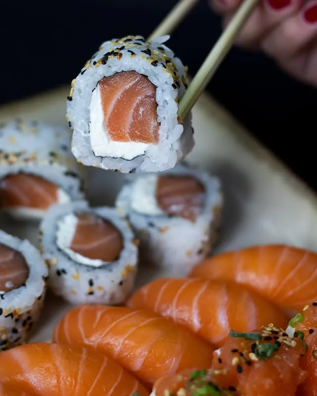 Uramaki de salmão sendo levantado com hashi sobre a travessa