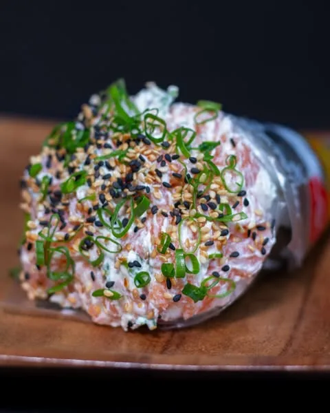 Temaki finalizado com cebolinha e gergelim sobre tábua de madeira