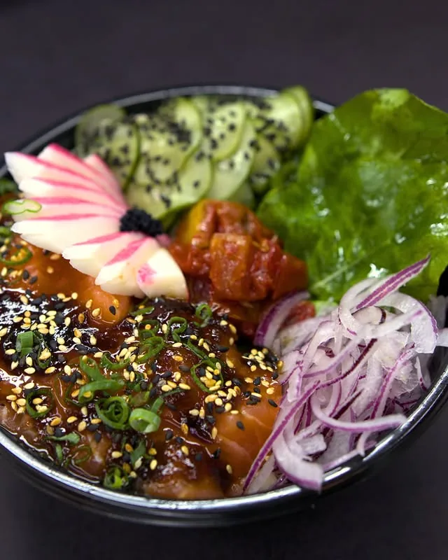 Tigela de poke com salmão, folhas e acompanhamentos do O Quinto Sabor