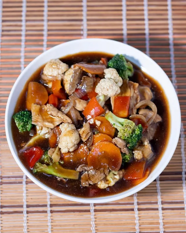 Yakisoba com legumes e pedaços de proteína em tigela sobre esteira de bambu